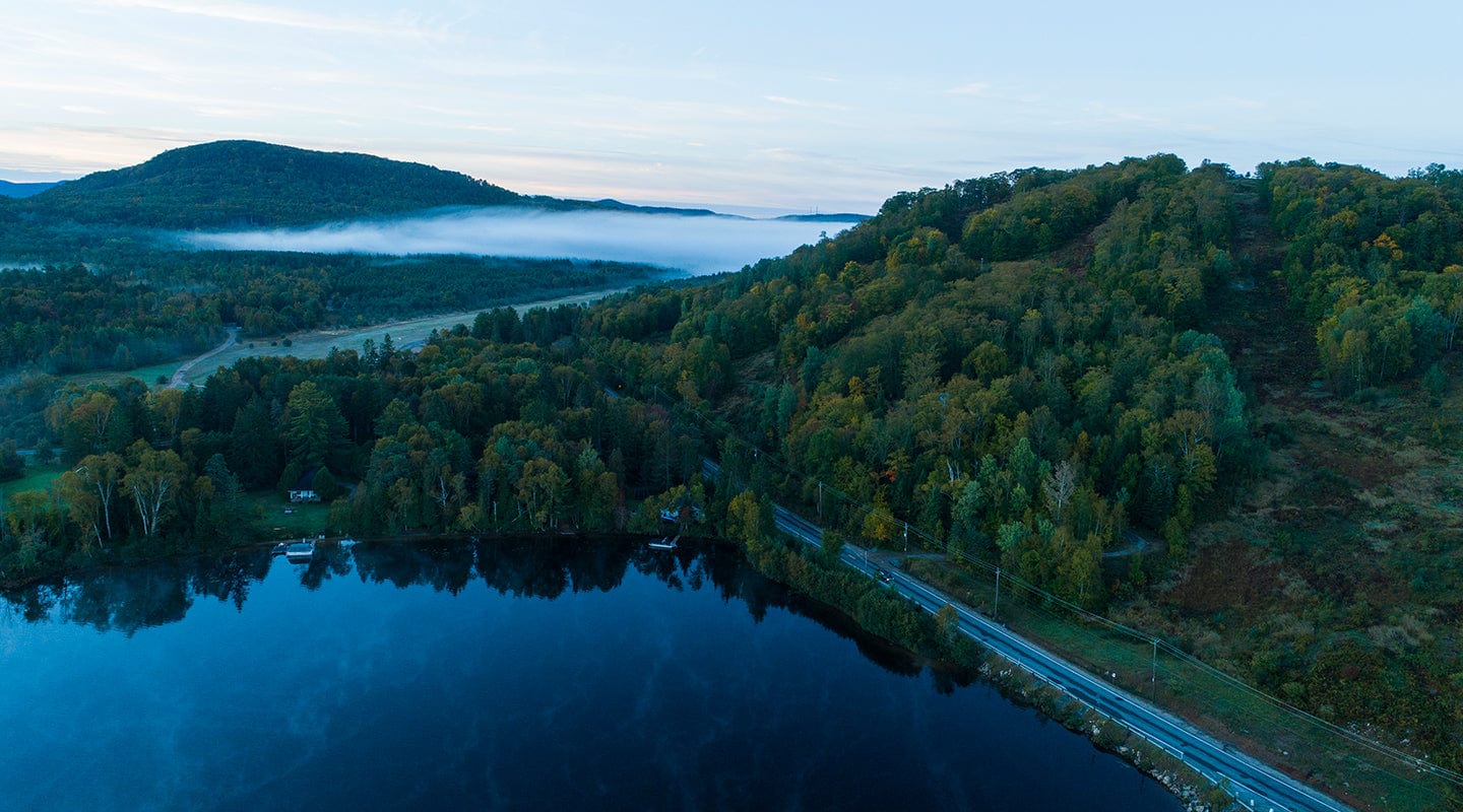 Aerial view of a forest, lake, and hills with morning mist.