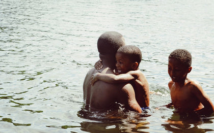 A dad is holding one child while another is next to them in the lake.