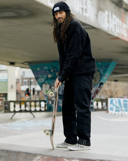 A person stands at a skatepark holding a skateboard.