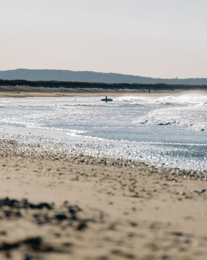 A person is walking with a surfboard along the shoreline.
