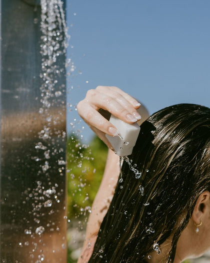 A person is washing their hair with a bar under an outdoor shower.