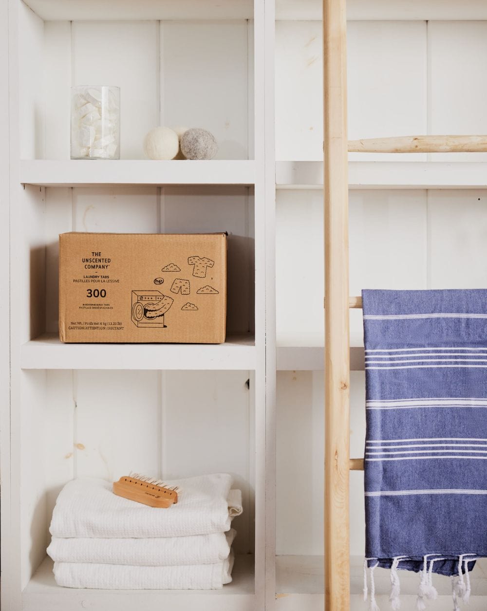 Box of The Unscented Company laundry tabs on a white shelf next to towels and dryer balls.
