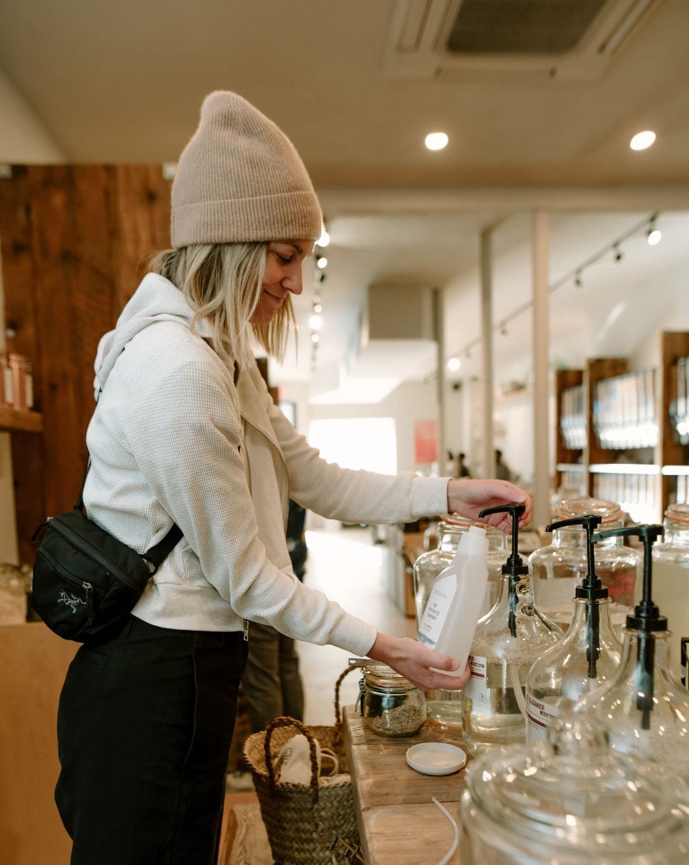 Woman refilling a bottle of The Unscented Company product at a bulk store.
