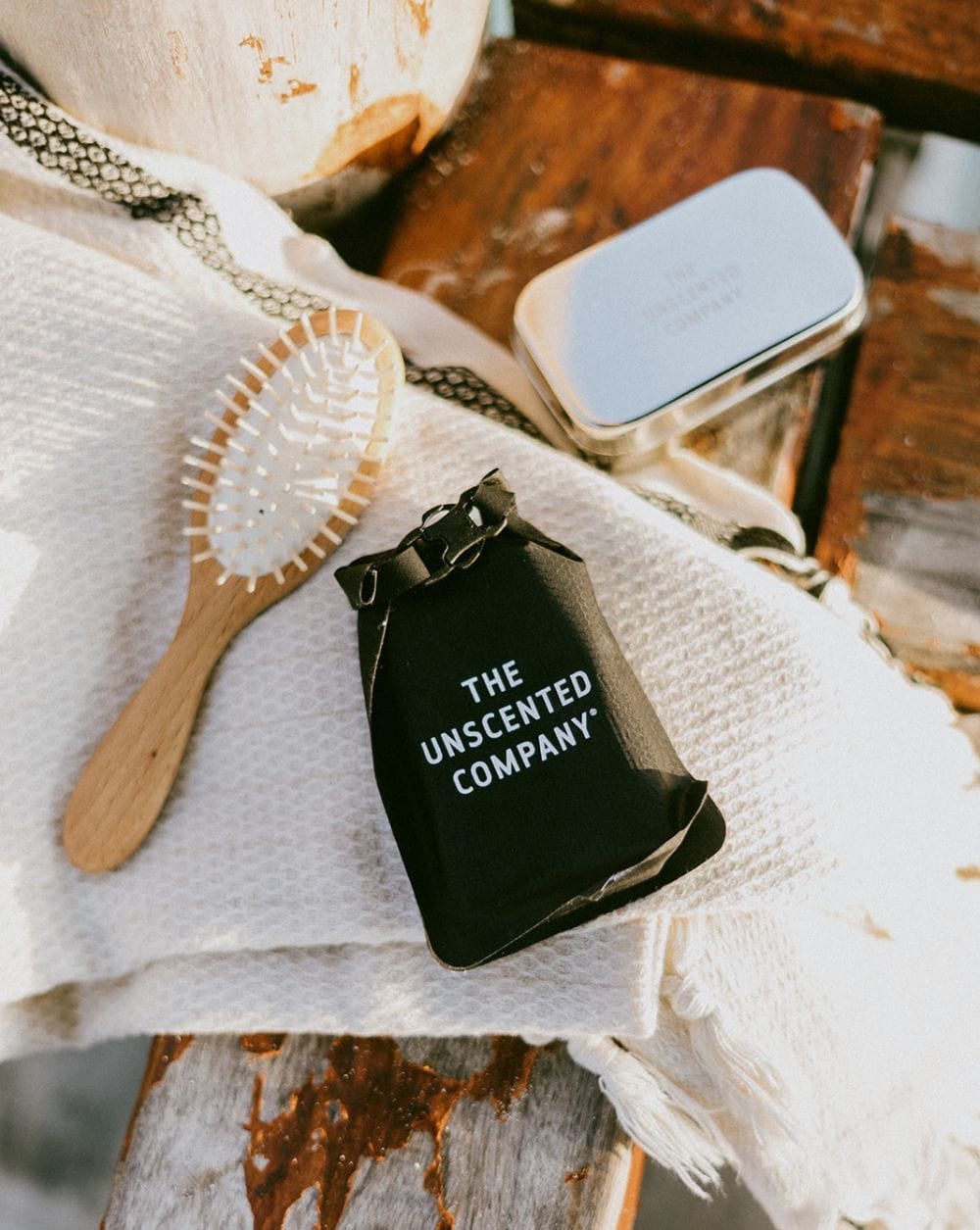 The Unscented Company shampoo bar with a wooden brush and tin on a white towel.
