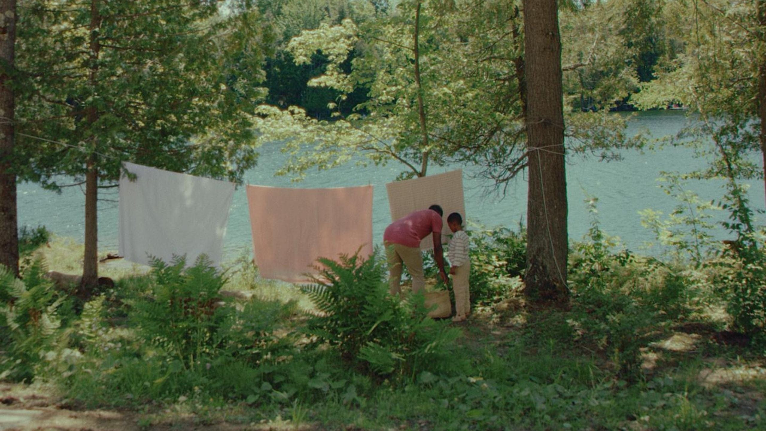 A man and child hanging laundry to dry by a lake in the forest.
