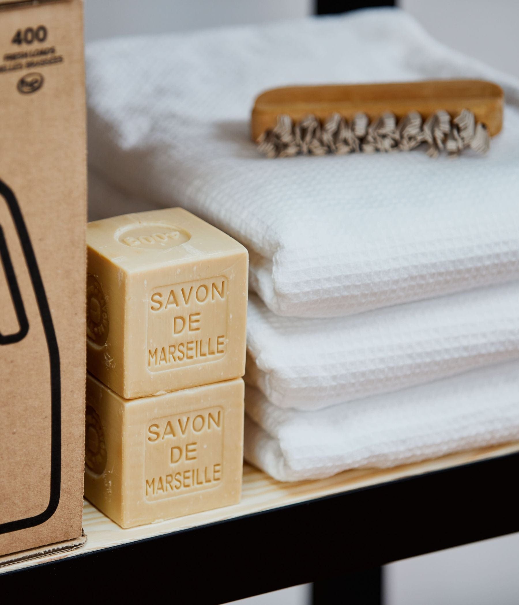 Two Savon de Marseille soap bars stacked next to folded white towels and a wooden nail brush.