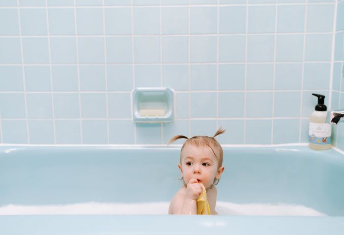 Toddler in the bath holding a yellow washcloth freshly washed with fragrance-free detergent