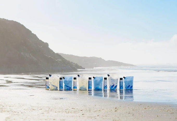 Row of shampoo and conditioner refill pouches lined up on a beach shoreline