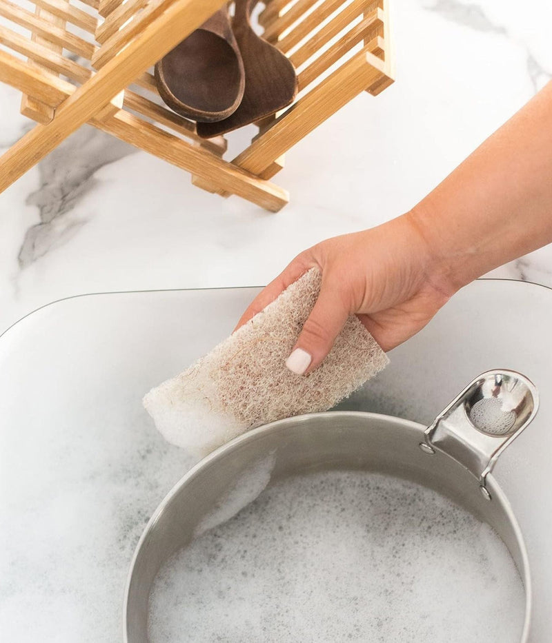 Hand washing a pot with a natural loofah sponge and soap suds.
