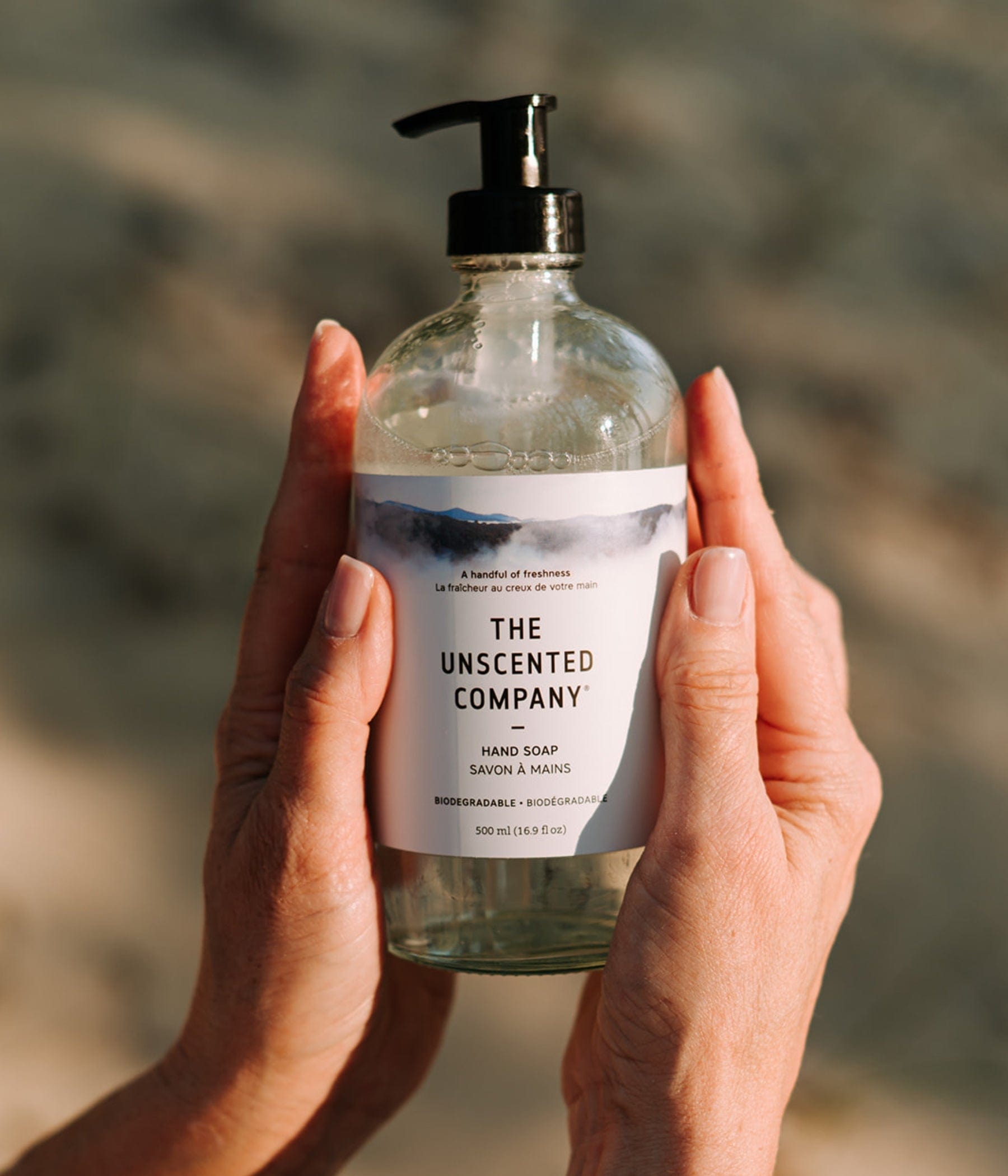A bottle of The Unscented Company hand soap held with both hands in soft light.