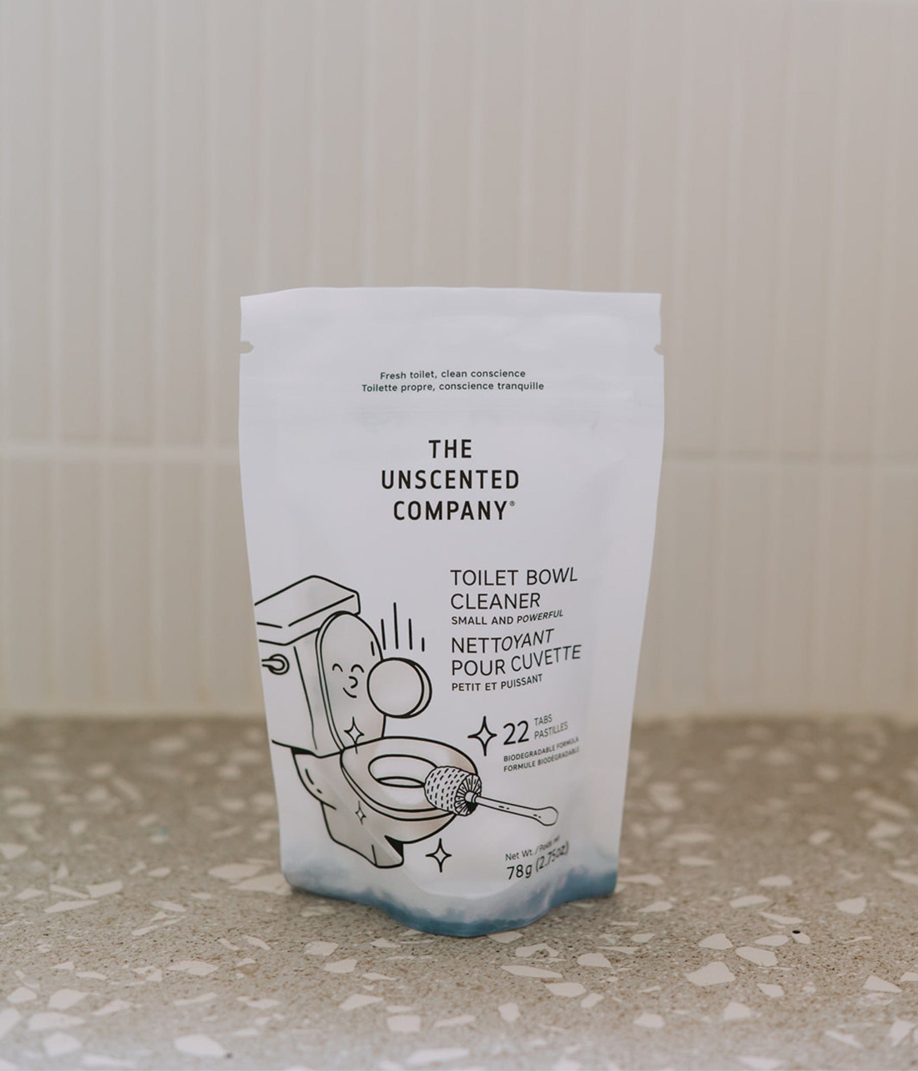 A pouch of The Unscented Company toilet bowl cleaner (22 tabs) placed on a terrazzo bathroom counter, in front of a white tiled wall.