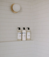 The Body Soap - 1L, the Daily Conditioner - 1L and the Daily Shampoo - 1L placed on a shower ledge.