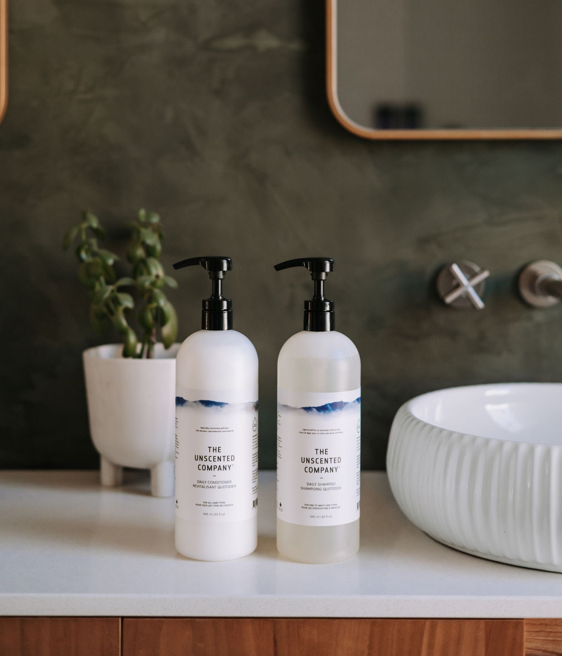 The Daily Conditioner - 1L and the Daily Shampoo - 1L placed a bathroom counter, on the left side of a sink, dark green background.