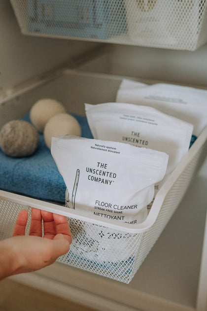 Close-up of a hand opening a white mesh drawer containing floor cleaner pacs and wool dryer balls.