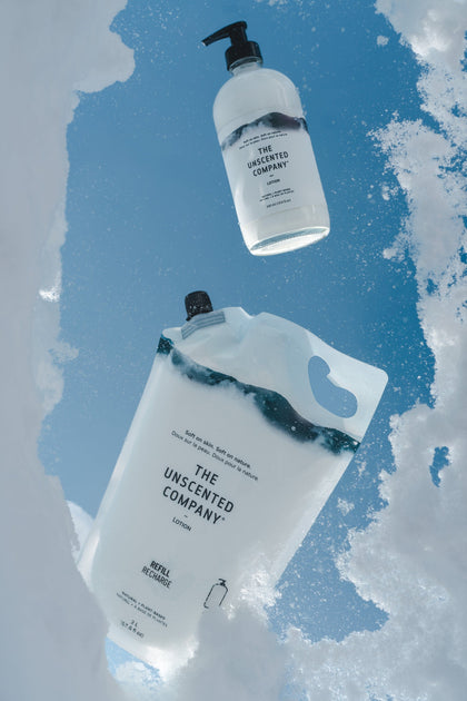 A bottle and refill pouch of The Unscented Company lotion placed in a snow opening, with a vivid blue sky in the background.