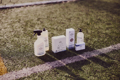 Range of The Unscented Company products neatly aligned on a soccer field, captured in morning light.