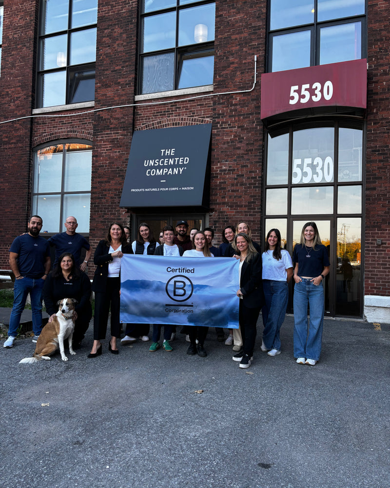 Team from The Unscented Company standing outside their Montreal headquarters at 5530 rue Saint-Patrick holding a Certified B Corporation banner, highlighting the company’s commitment to sustainability and responsible business.
