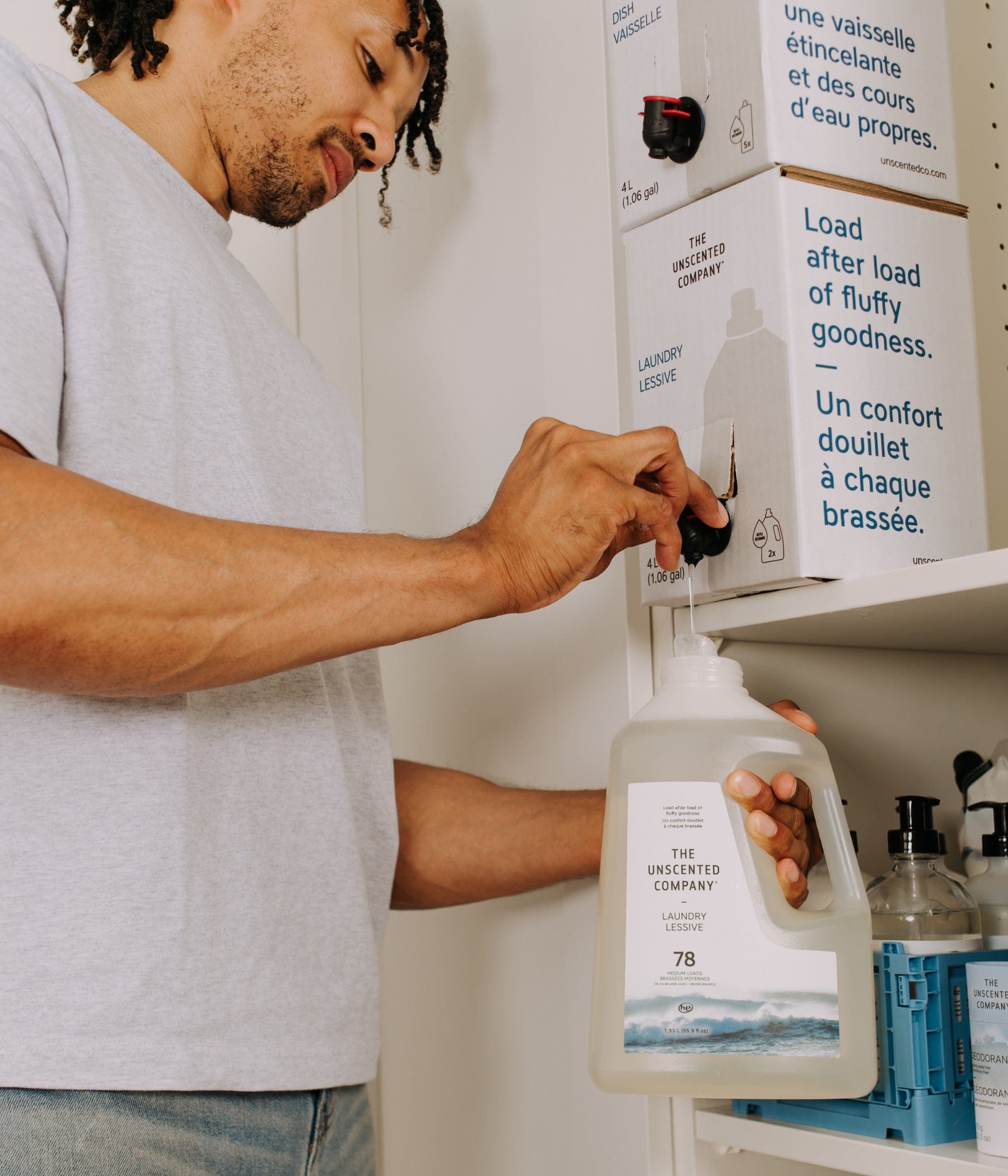 Man refilling a laundry detergent bottle from a The Unscented Company 4L bulk refill station box mounted on a shelf in a modern laundry room.