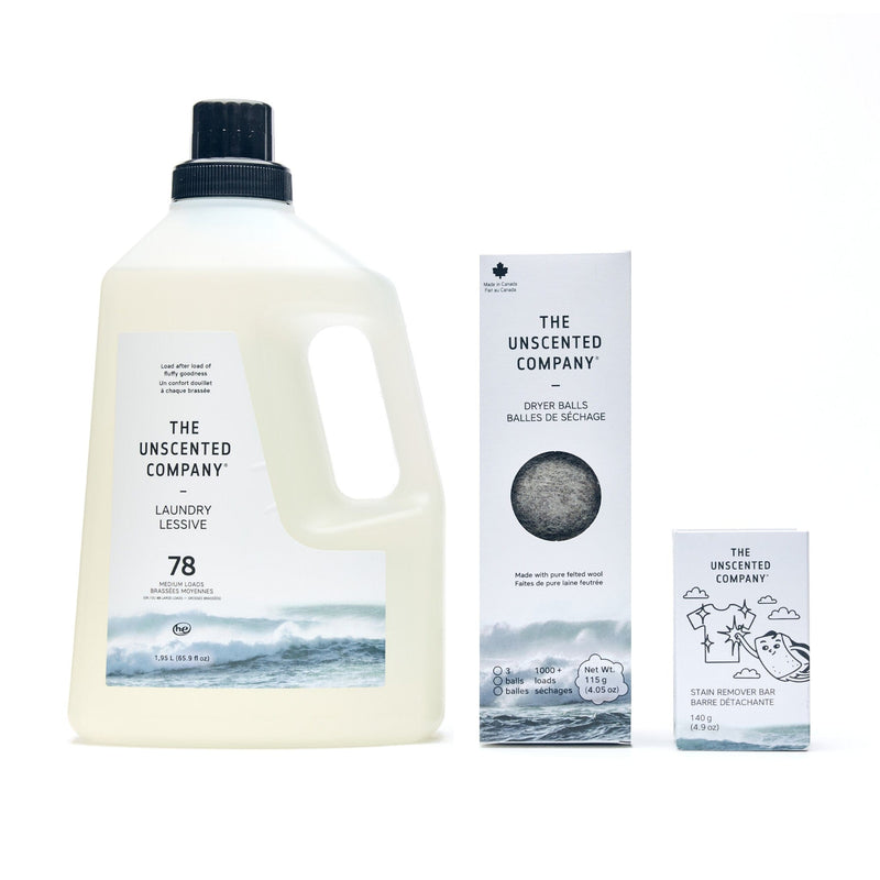 A product lineup of The Unscented Company essentials on a white background, featuring a 1.95 L jug of liquid laundry detergent (78 loads), a box of wool dryer balls, and a 140 g stain remover bar.