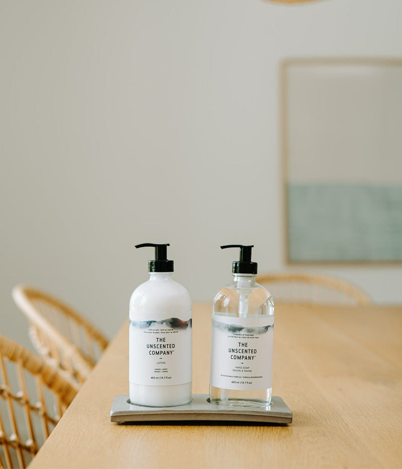 Fragrance-free hand soap and lotion from The Unscented Company in reusable glass bottles, displayed on a wooden table in a bright, minimalist dining room.