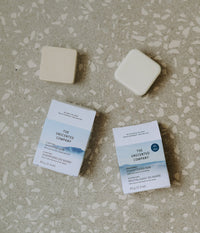The Unscented Company solid shampoo and conditioner bars with their packaging, displayed on a terrazzo surface — fragrance-free and plastic-free hair care.
