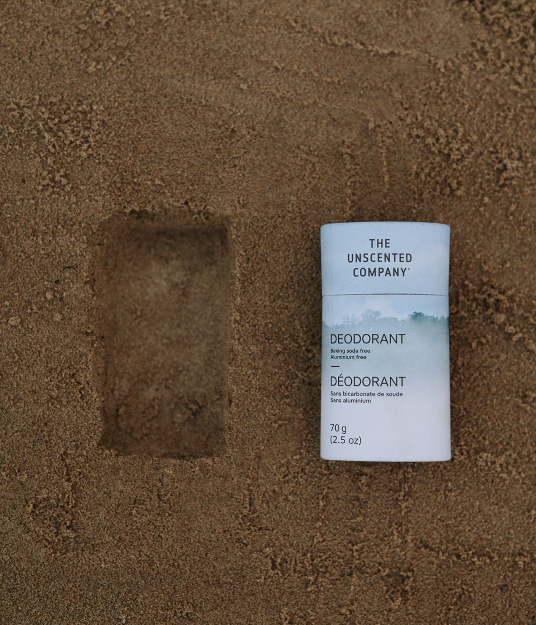 Aluminum-free deodorant from The Unscented Company resting on sand next to its imprint.