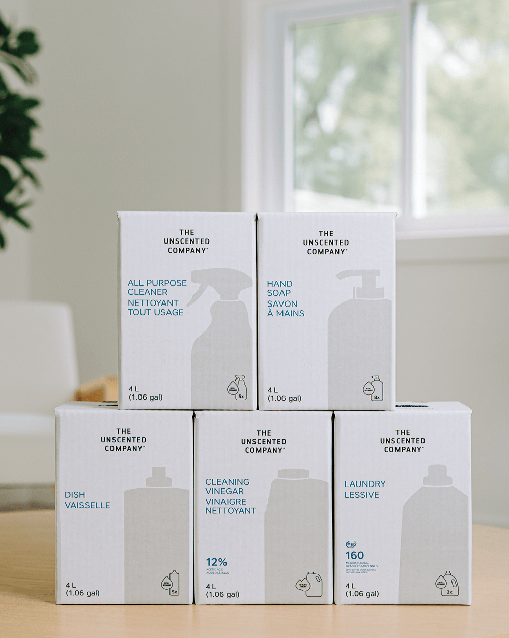 Stack of The Unscented Company refill boxes on a table, including All-Purpose Cleaner, Hand Soap, Dish Soap, Cleaning Vinegar, and Laundry Detergent, showcasing fragrance-free, eco-friendly home cleaning products.
