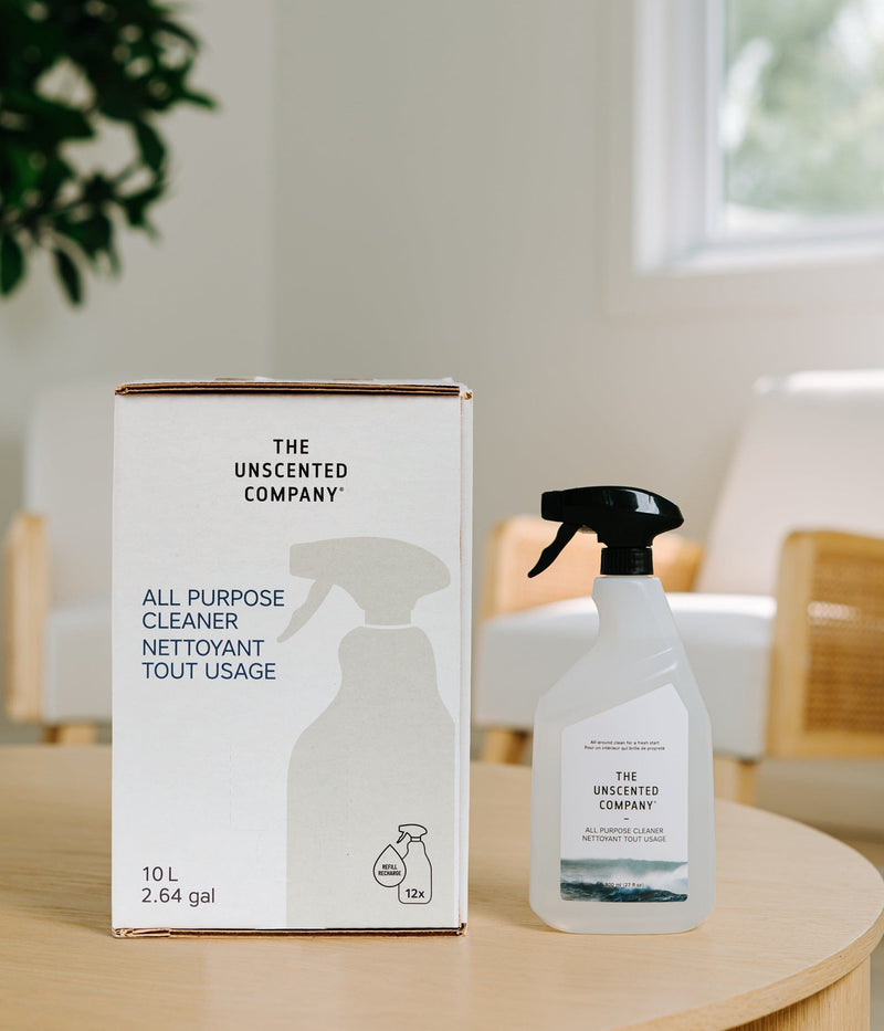 10 L (2.64 gal) refill box and spray bottle of The Unscented Company All Purpose Cleaner displayed on a wooden table in a bright kitchen, featuring minimalist white packaging, “ALL PURPOSE CLEANER / NETTOYANT TOUT USAGE” text, and 12x refill icon.