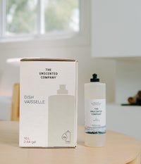 Refill box and bottle of The Unscented Company Dish / Vaisselle dish soap on a wooden table, showing 10 L (2.64 gal) refill packaging with 13x refill icon and 750 ml bottle, photographed in a bright minimalist kitchen.
