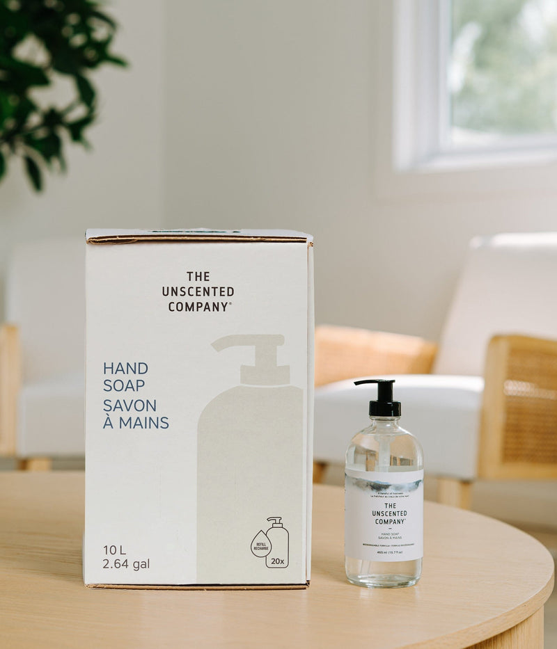 10 L (2.64 gal) refill box and pump bottle of The Unscented Company Hand Soap displayed on a wooden table in a bright kitchen, featuring minimalist white packaging, “HAND SOAP / SAVON À MAINS” text, and 20x refill icon.