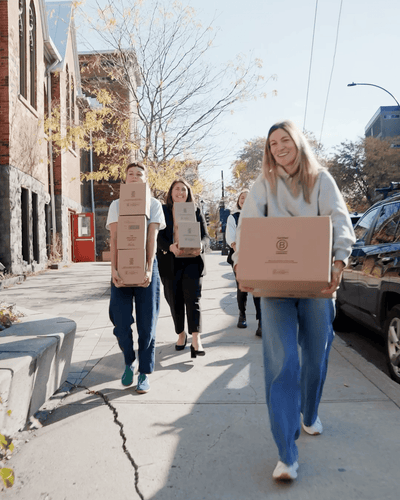 Team members from The Unscented Company carrying product boxes along a city street, highlighting sustainable logistics and the growing distribution of eco-friendly household products.
