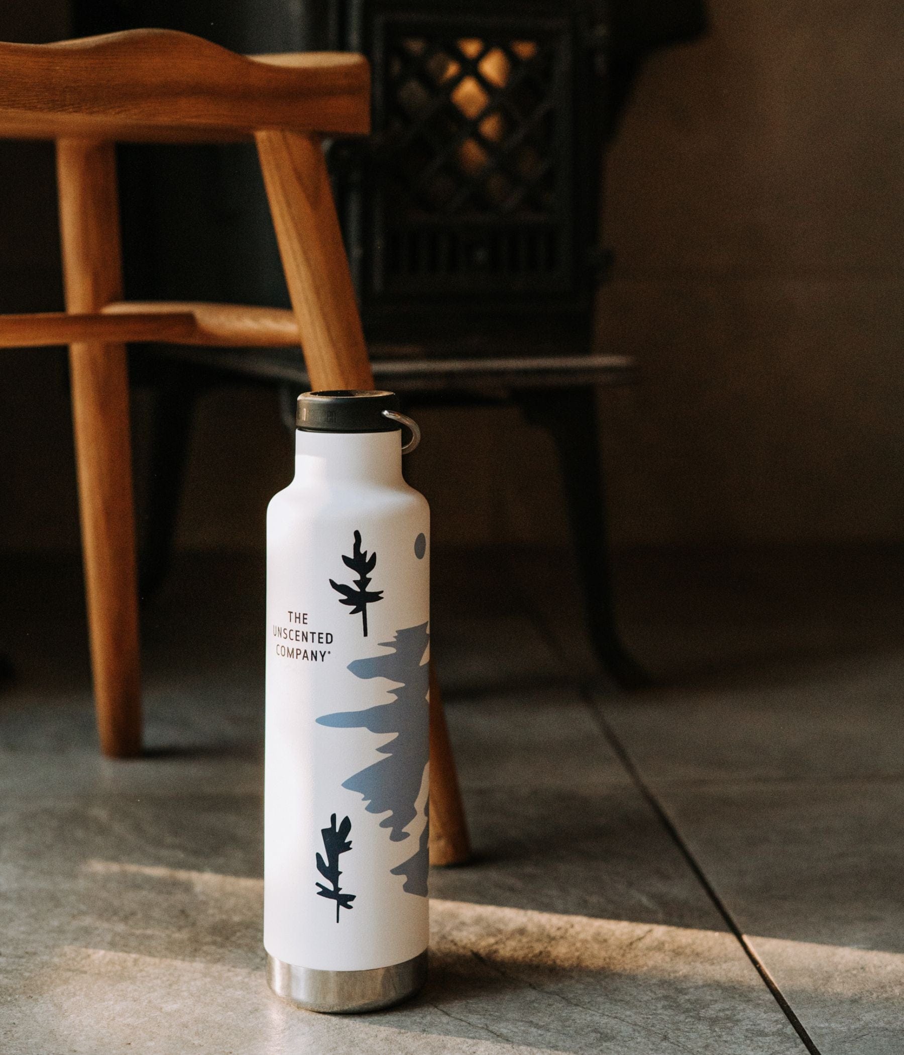 The Unscented Co. Insulated Bottle X Kleen Kanteen placed on the floor, a wooden stool in the background.